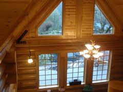Depicted here is a chandelier-style light fixture hanging high in the air inside a log cabin double decker home that is located in Clifton, Virginia.